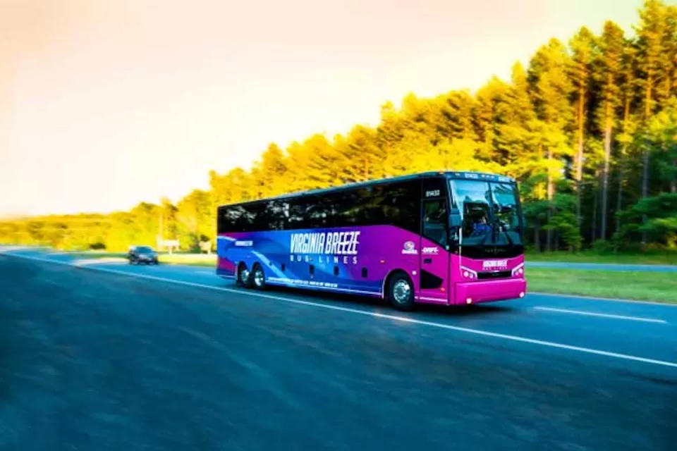Purple Virginia Breeze intercity bus driving down blurred road with trees on roadside.